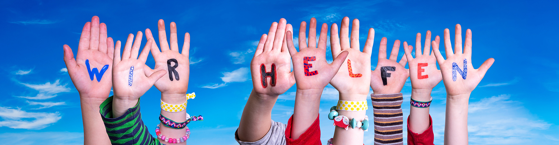 Kinderhände halten bunte Buchstaben in die Höhe, aus denen sich das Wort "Wir helfen" zusammensetzt; es handelt sich um das lizenzierte Stockfoto Nr. 335502821 von Nelos